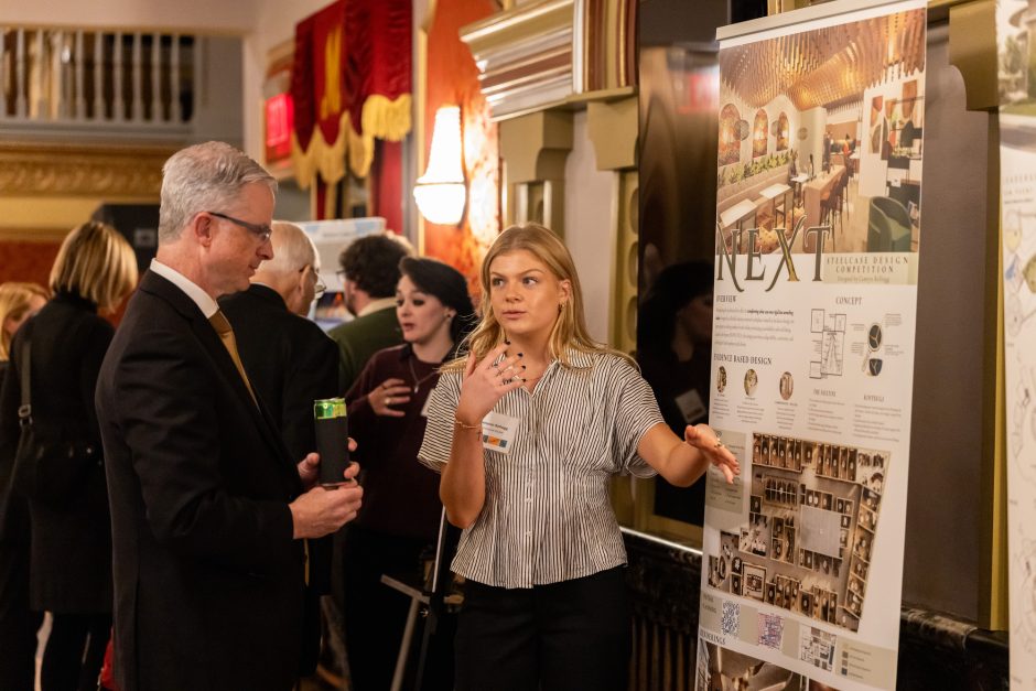 Student presents poster board of art project to university official