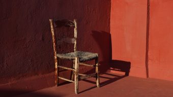 Old wooden one vintage chair in a room with red grunge walls and floor in sunlight, dark shadows.