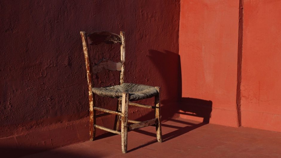 Old wooden one vintage chair in a room with red grunge walls and floor in sunlight, dark shadows.