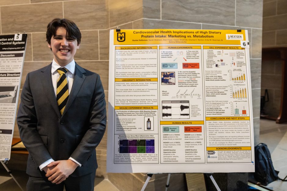 Student wearing gray suit standing next to research poster