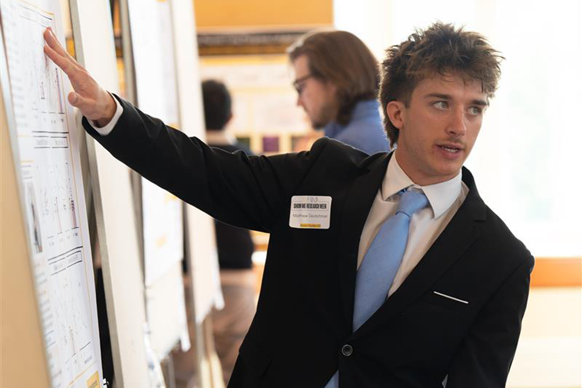 Student in tie points to poster