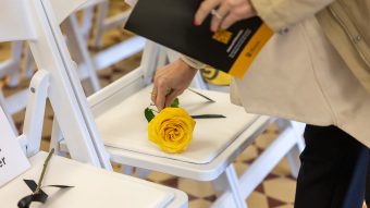 A person's hand placing a yellow rose on a white chair
