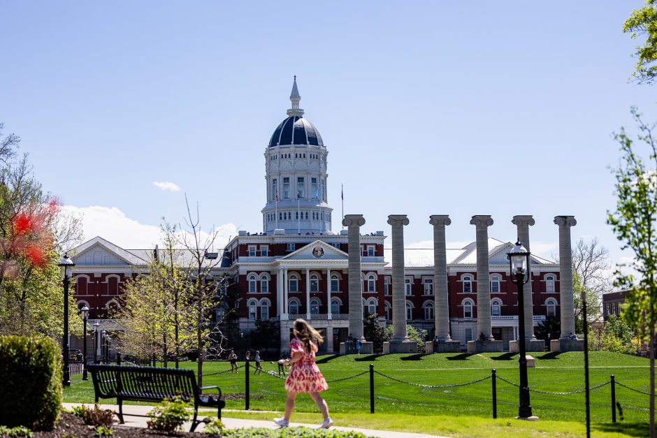 Student walking on around Francis Quadrangle with the Columns and Jesse Hall in the background