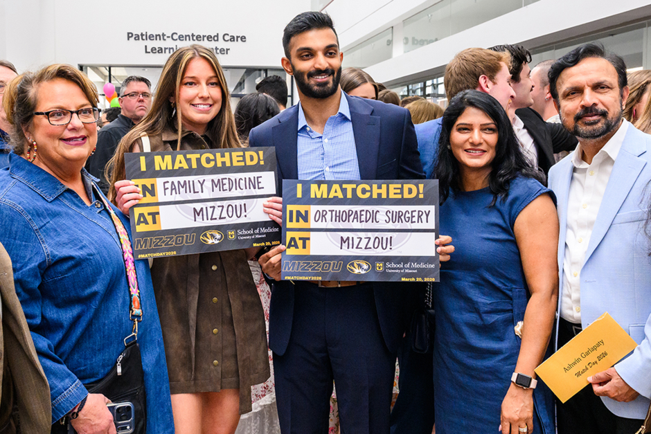 Two medical school students holding Match Day signs with family.