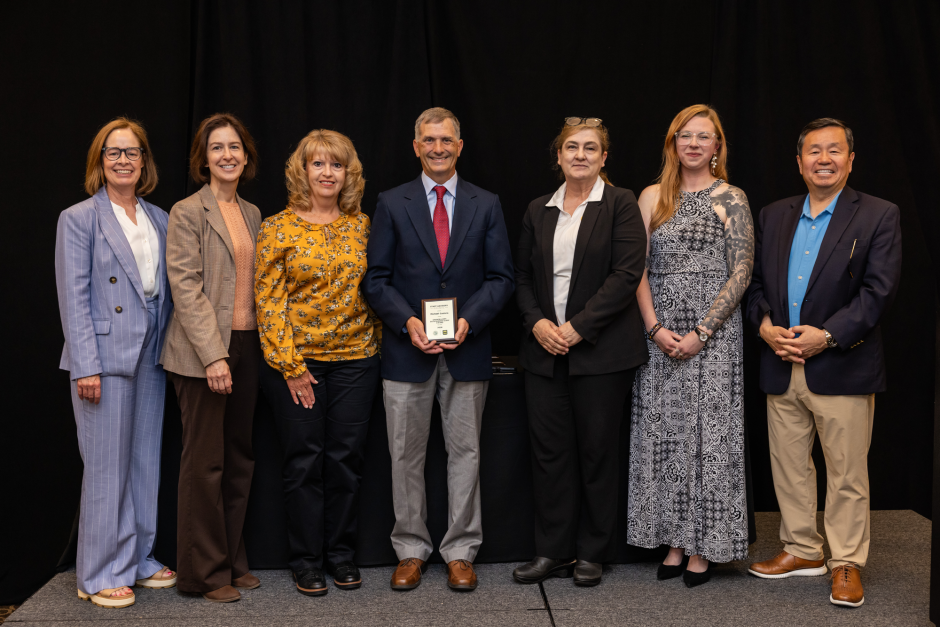 Michael Castera holds award with university leaders
