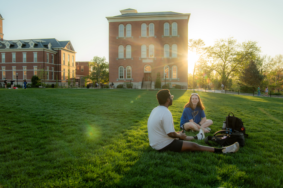 Two people sit in grass on sunny day