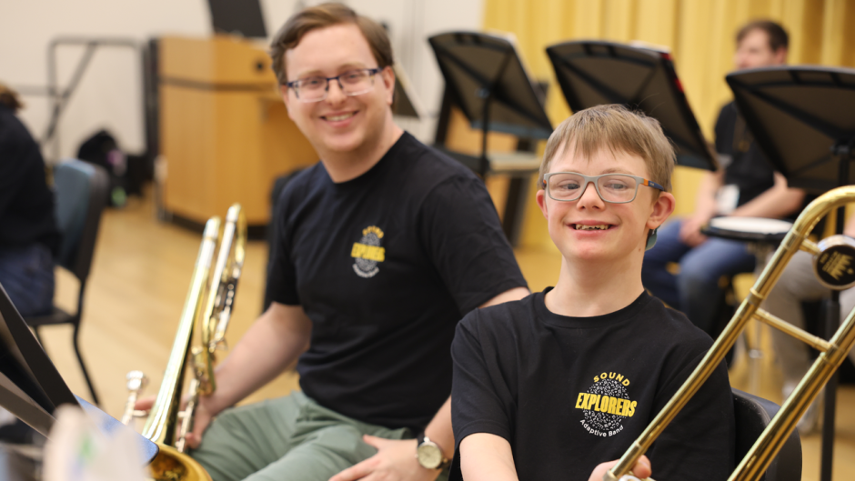 A child with a horn sits next to a mentor musician