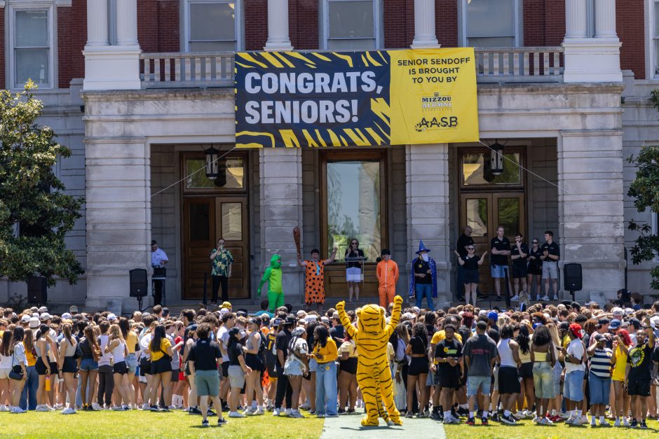 Truman the Tiger with arms raised in front of a large group of students