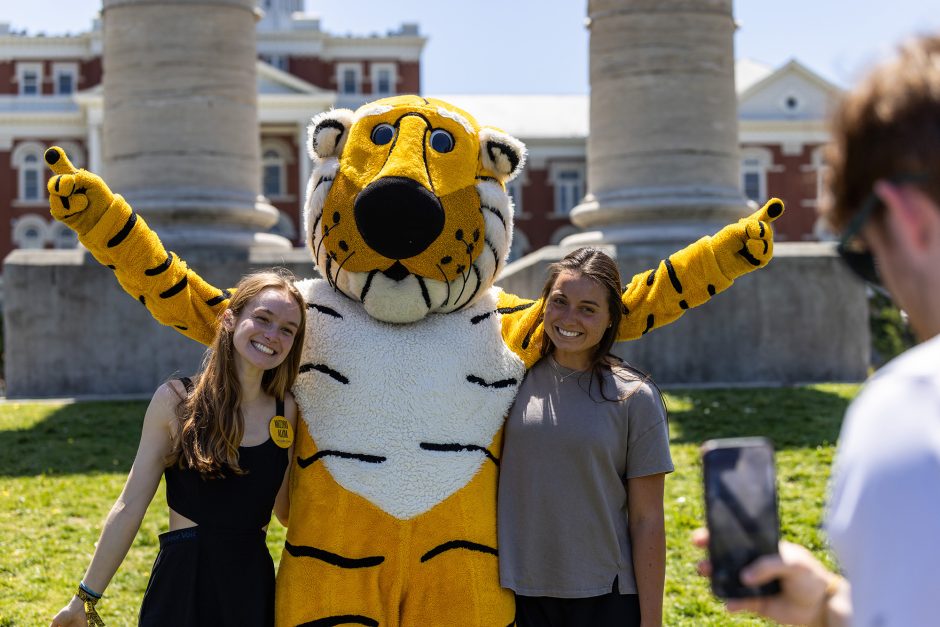 Two students posing for a photo with Truman the Tiger in front of the Columns