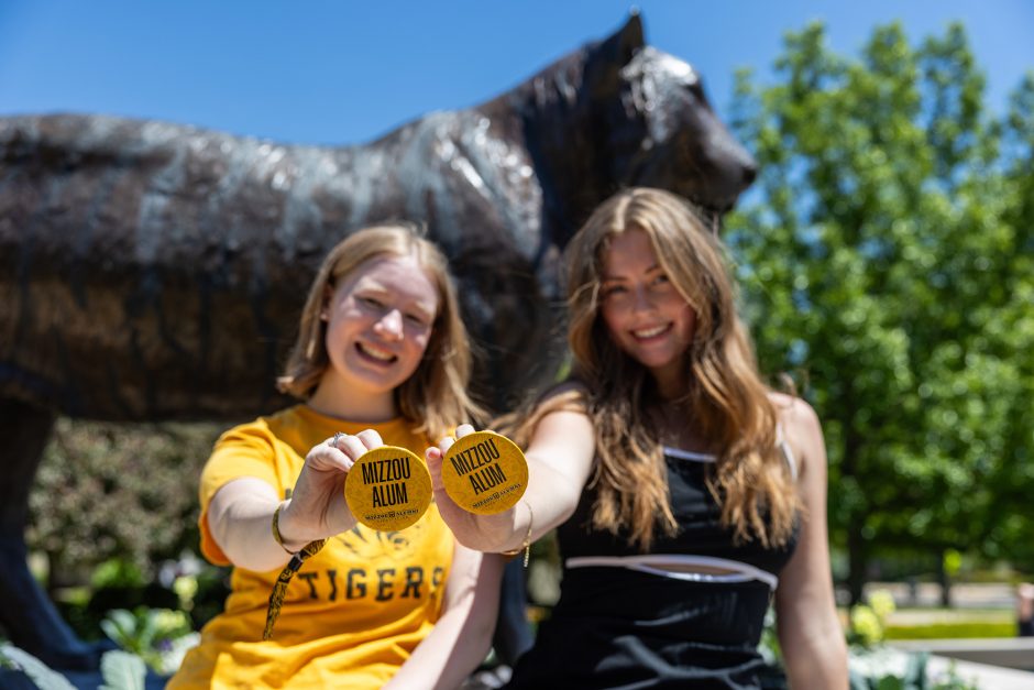 Two students holding up buttons that say "Mizzou Alum"