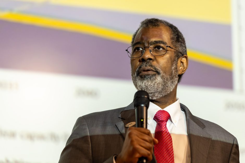 A person wearing a suit and red tie speaking into a microphone