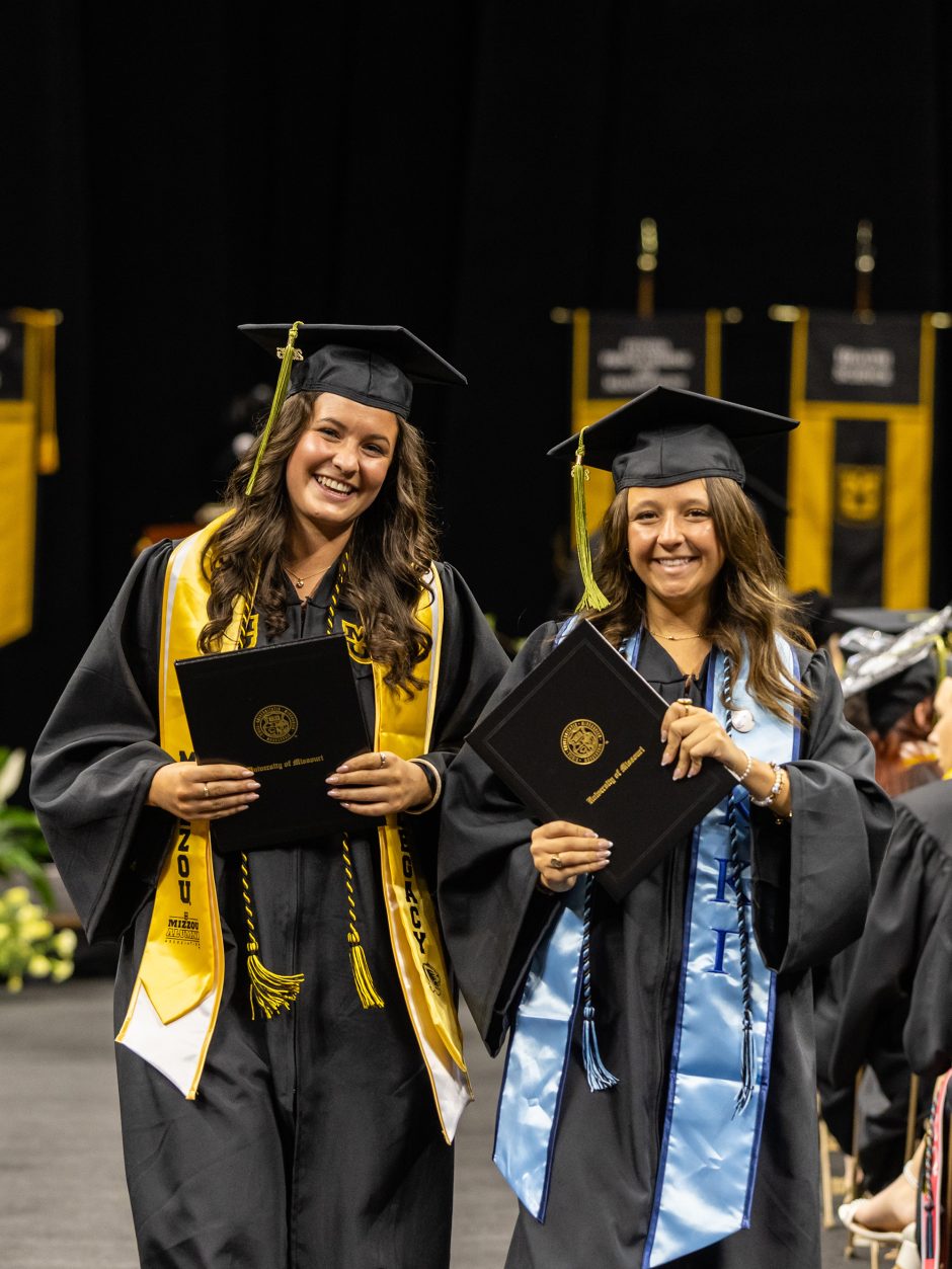 Two graduates show off their diplomas