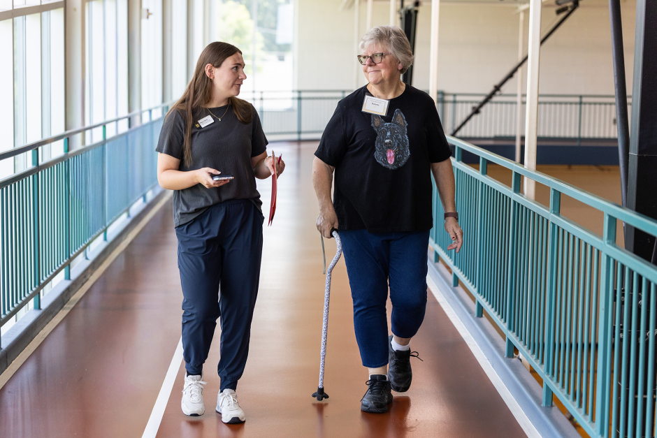 A health care worker walks next to a woman with a cane