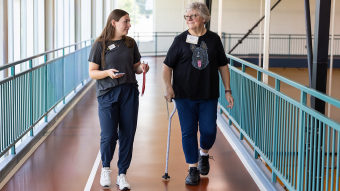 A health care worker walks beside a woman with a cane