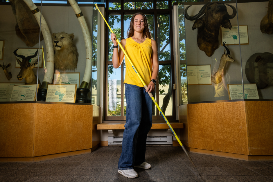 Skylar Ciccolini holds her javelin while standing in front of a display of animal heads in the school of natural resources