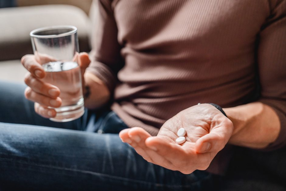 Person holding aspirin in one hand and glass of water in the other
