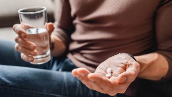 Person holding aspirin in one hand and glass of water in the other
