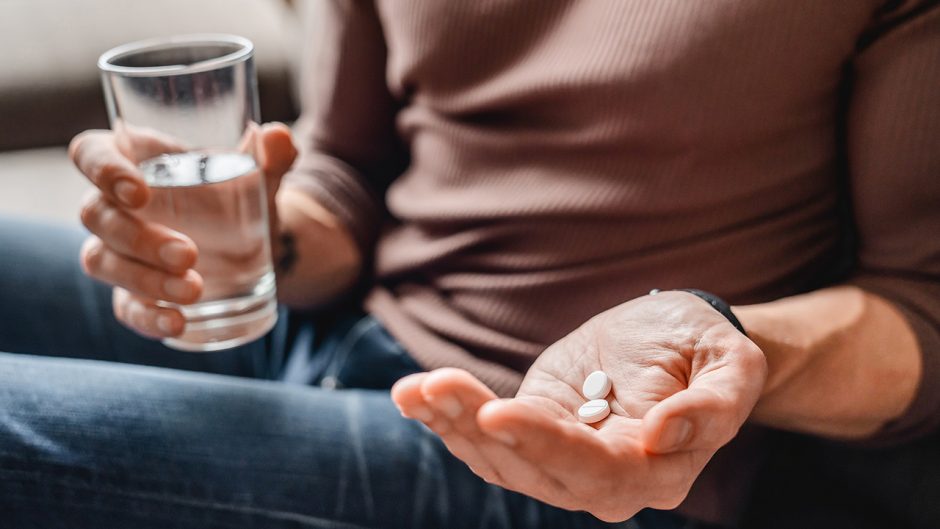 Person holding aspirin in one hand and glass of water in the other