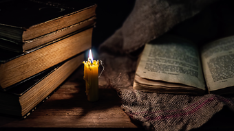 A candle burns near old books