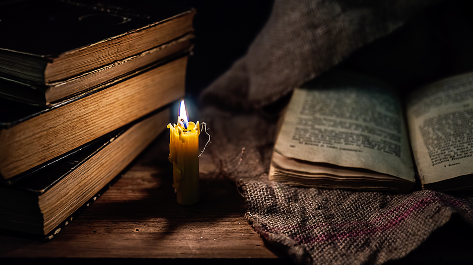 A candle burns near old books