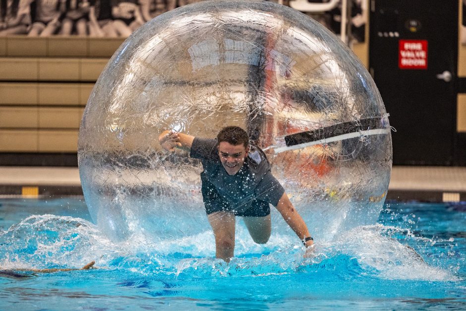 Student running across the surface of a pool inside a large inflatable ball