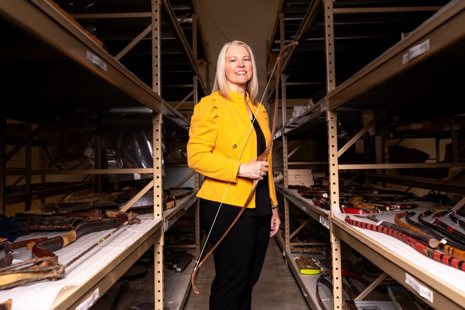 Candace Sall stands with her competition bow among shelves of archery artifacts that make up Mizzou's Grayson Archery Collection