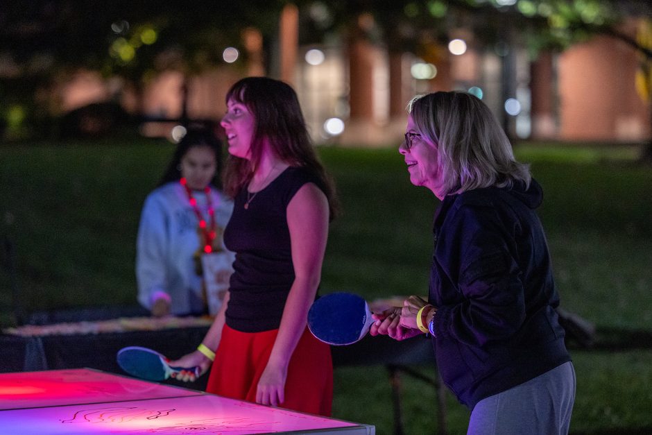 Two people playing ping pong outside at night
