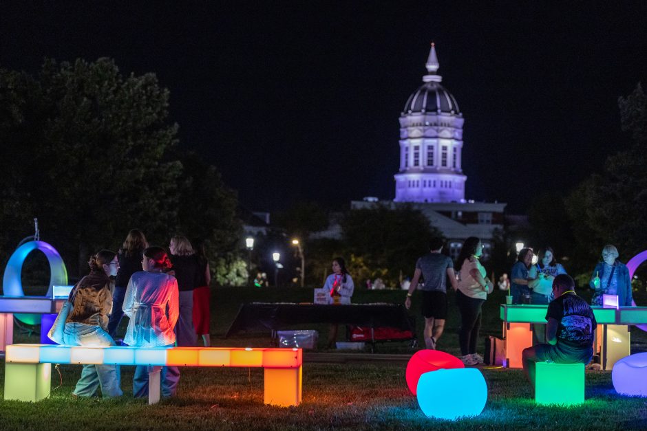 People at nighttime outdoor event with Jesse Hall illuminated in the background