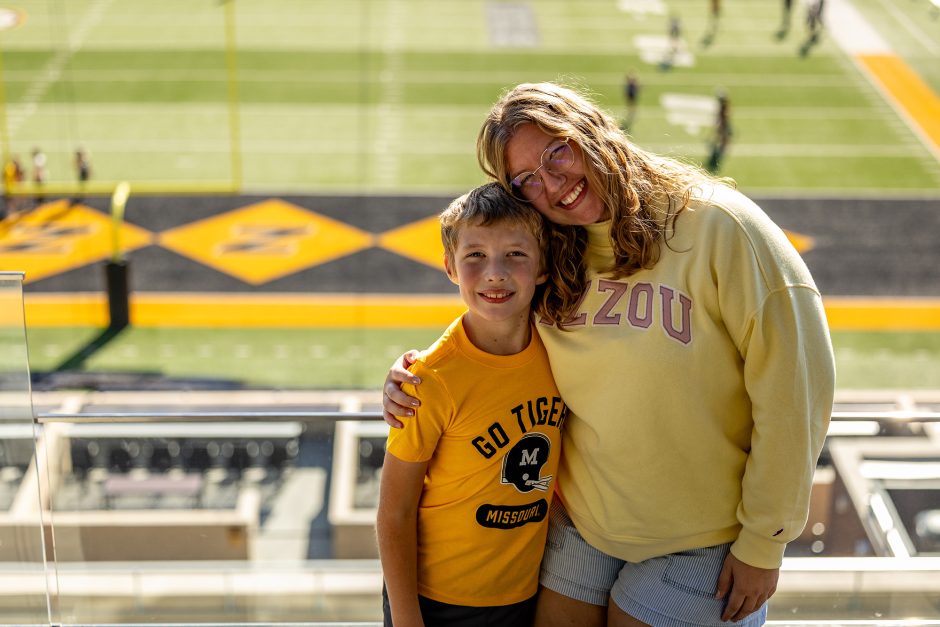 Two people posing for photo with football field in the background
